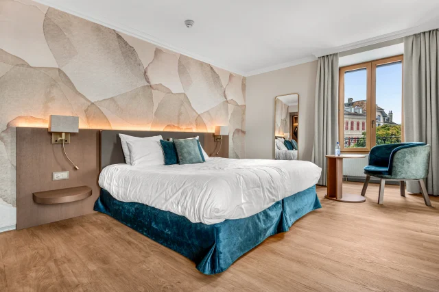 La chambre de l’Hôtel Le Rive, son lit et son mobilier en bois face aux fenêtres