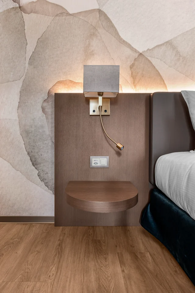 Le chevet arrondi, l’applique et le papier peint de la chambre