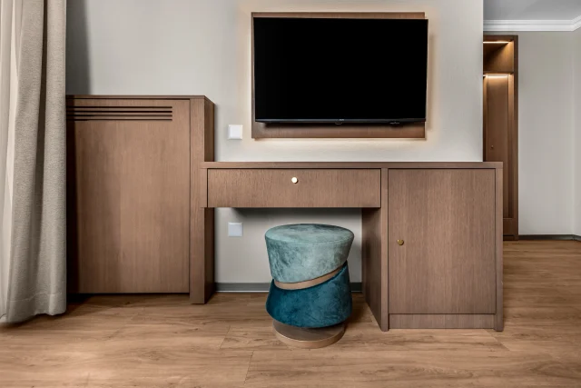 Le meuble TV en bois, le bureau et l’assise turquoise de l’Hôtel Le Rive